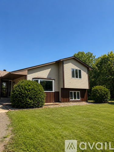 A house with a brown and beige exterior is surrounded by green grass and trees.
