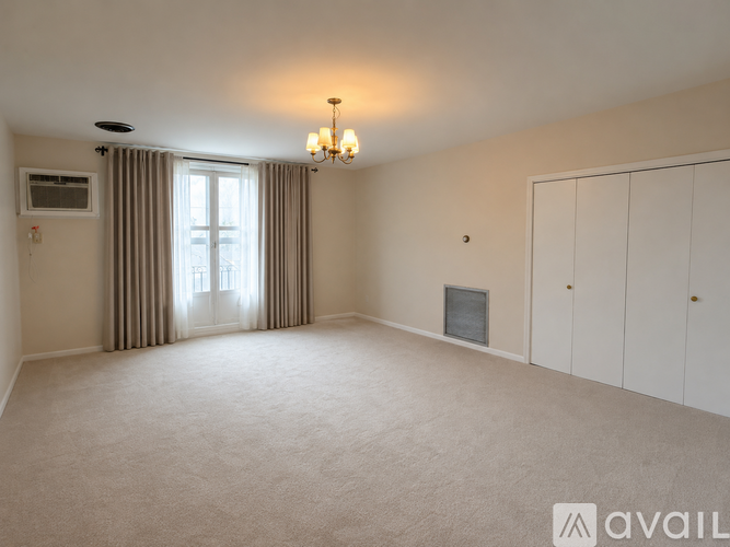 A spacious room with a window, curtains, a chandelier, and a fireplace.