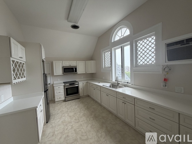 A kitchen with white cabinets and appliances, a window with white shutters, and a tiled floor.