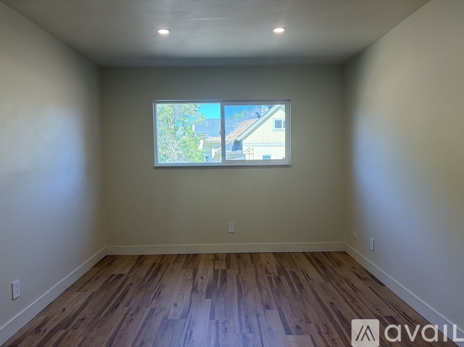 A room with wooden flooring and a window showing a view of a house.