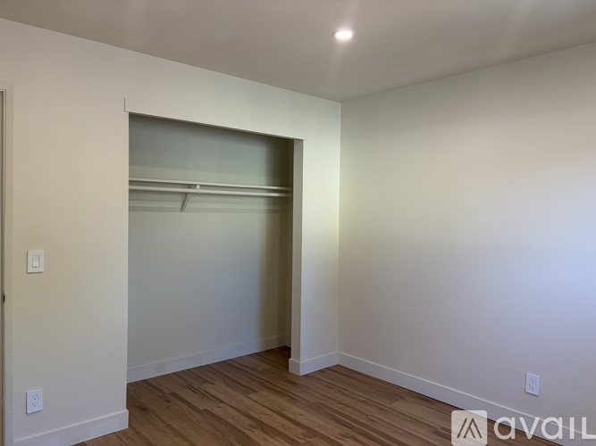 A room with a white wall and a wooden floor with a doorway leading to another room.