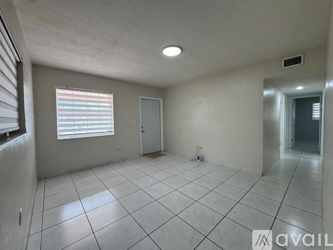 A spacious room with tiled flooring and a window with blinds.
