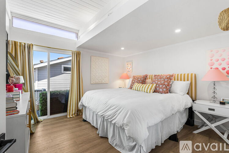 A bedroom with a large bed and a balcony with a view of the backyard.