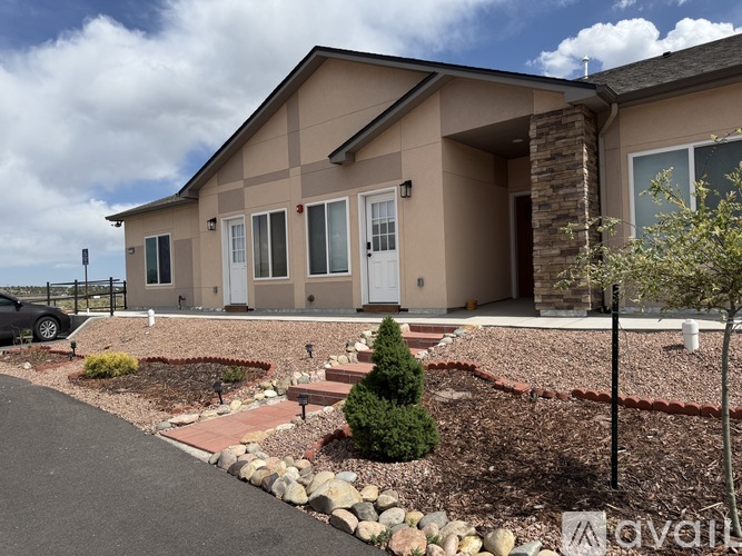A beige house with a white door and windows, surrounded by a gravel driveway and landscaping.