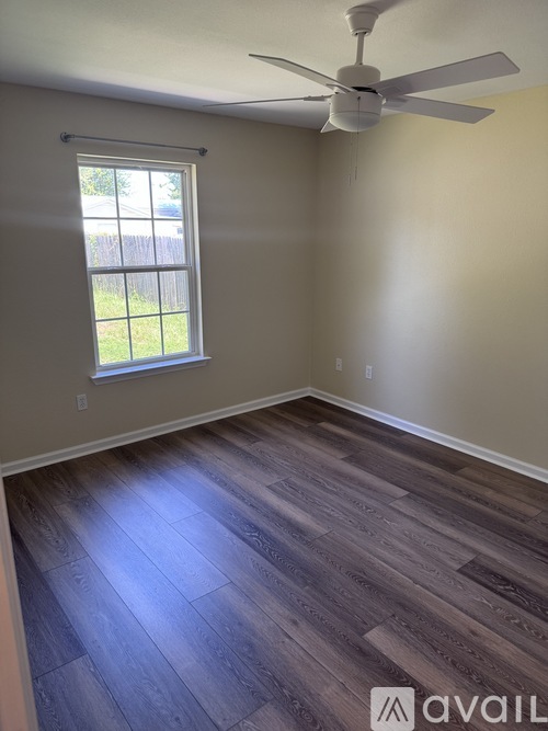 A room with a ceiling fan and a window with a view of a fence and trees.