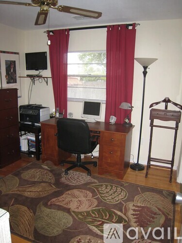 A room with a desk, chair, and a fan.