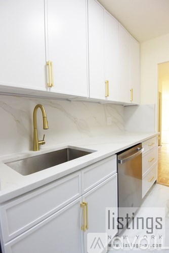 A kitchen with white cabinets and a marble backsplash.