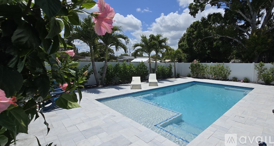 A pool surrounded by greenery and a white fence.
