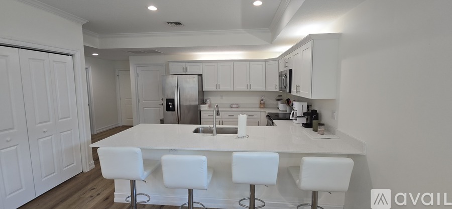 A kitchen with white countertops and white bar stools.