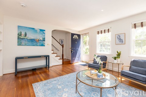 A living room with a blue rug and a painting on the wall.