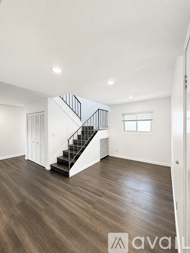 A spacious room with wooden flooring and a staircase with a metal railing.