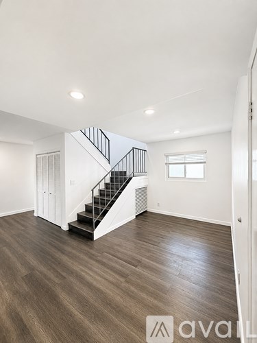 A spacious room with wooden flooring and a staircase with a metal railing.