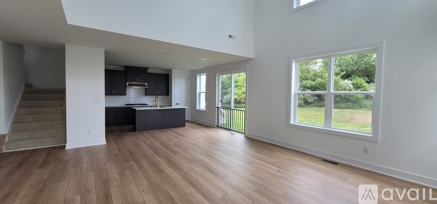A spacious living room with wooden flooring and a large window overlooking a green outdoor area.