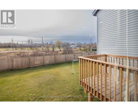 A wooden deck overlooks a grassy area with a fence and trees in the distance.