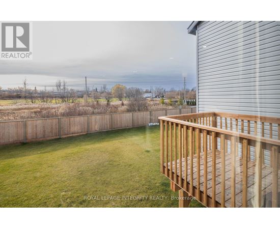 A wooden deck overlooks a grassy area with a fence and trees in the distance.
