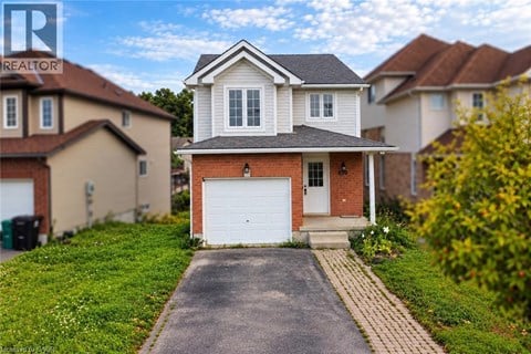 A white house with a grey roof is in the foreground with a driveway leading to a white garage door.