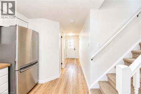 A stainless steel refrigerator sits in a kitchen with wooden floors and white walls.
