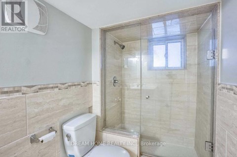A bathroom with a toilet, a glass shower stall, and a window.