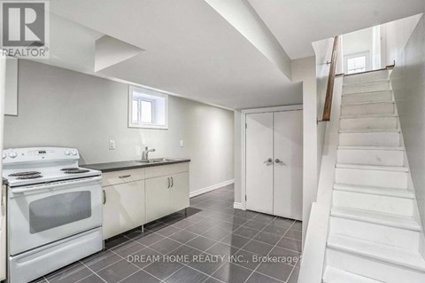 A white kitchen with a stove top oven and a staircase.