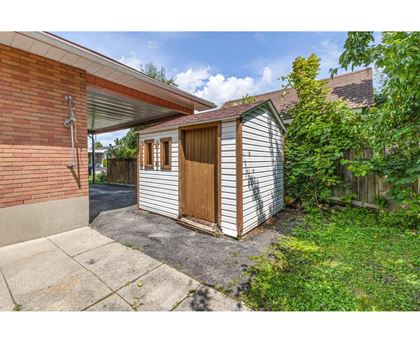 A small wooden shed with a brown door is attached to a brick house.