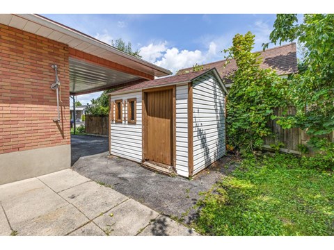 A small wooden shed with a brown door is attached to a brick house.
