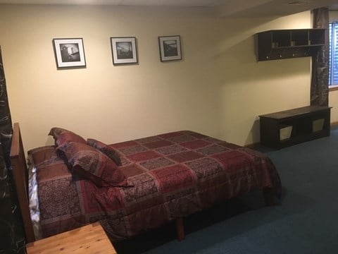 A bed with a red and grey comforter is in a room with three pictures on the wall.