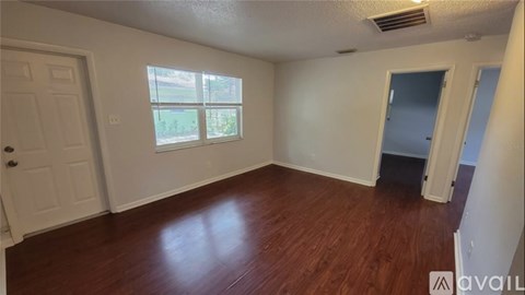 A room with wooden floors and a window with a view of a green area outside.