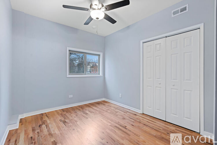 A room with a ceiling fan and a window with a view of trees and a building outside.