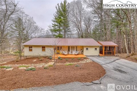 A house with a red roof is surrounded by trees and has a driveway leading to the front door.