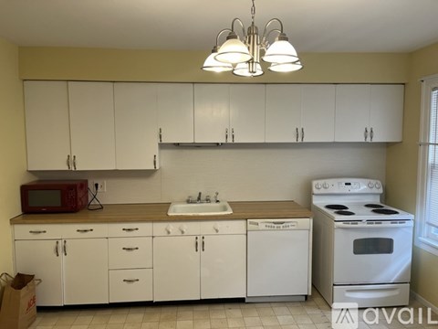 A kitchen with white cabinets and appliances, a red microwave, and a white stove.