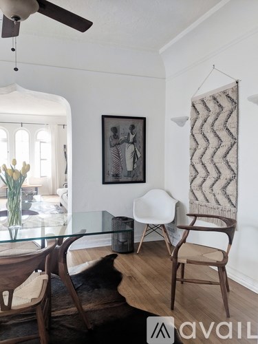 A living room with a glass table and chairs, a ceiling fan, and a hanging rug.