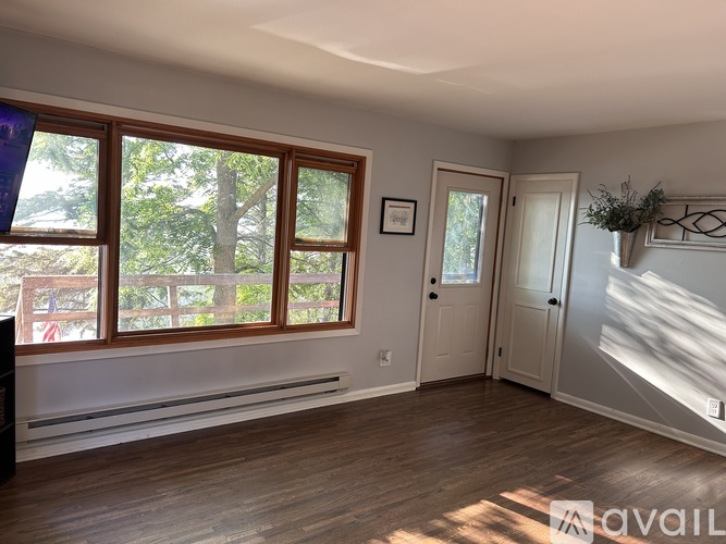 A room with wooden floors and a large window with a view of trees.