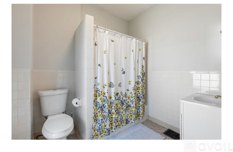 A white toilet is next to a shower curtain with a floral pattern.
