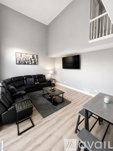 A living room with a black leather couch, a wooden coffee table, and a television mounted on the wall.