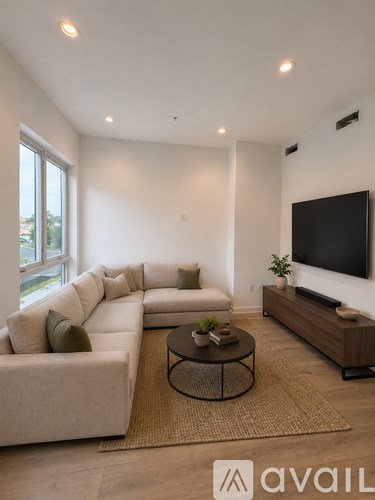 A living room with a white couch, a coffee table, and a flat screen TV mounted on the wall.
