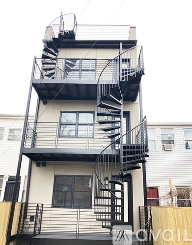 A black metal staircase with a balcony is attached to a white building.