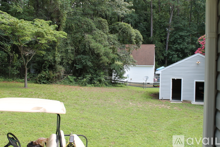 A white shed sits in a grassy yard next to a tree.