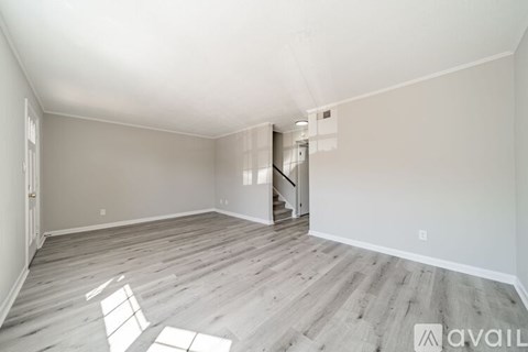 A spacious room with wooden flooring and a staircase in the background.