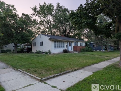 A house with a white exterior and a blue door is surrounded by trees and grass.