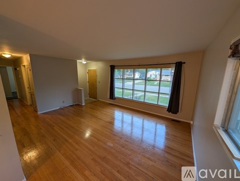 A room with wooden flooring and a large window with a view of the street outside.