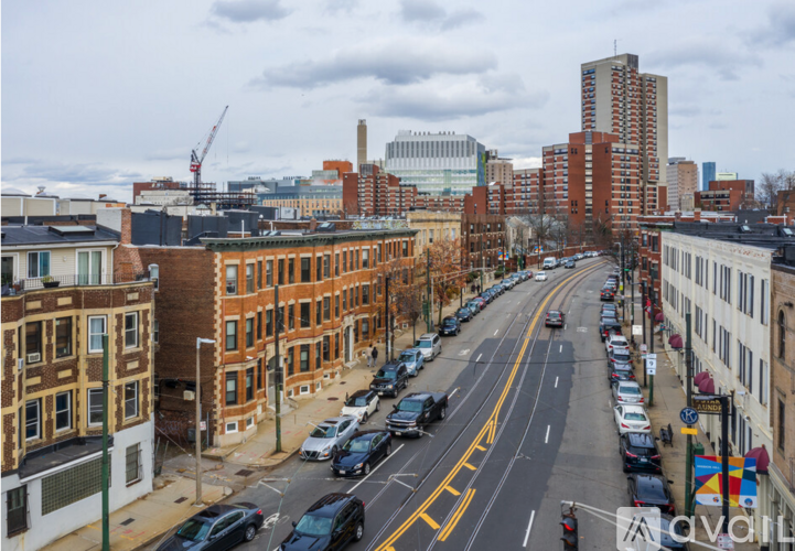 A city street with cars parked on the side and buildings in the background.