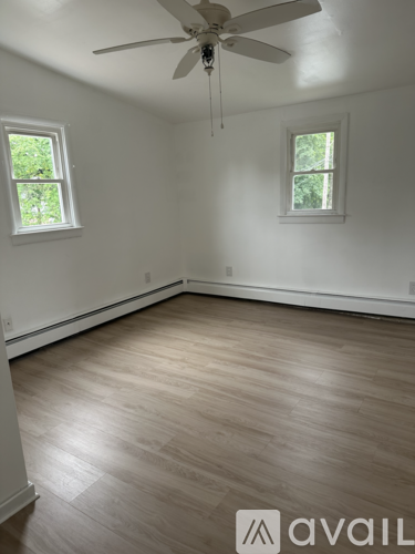A room with a ceiling fan and two windows.