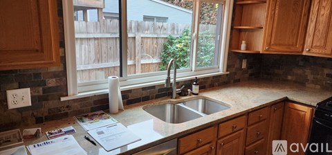 A kitchen with wooden cabinets and a window overlooking a fence.