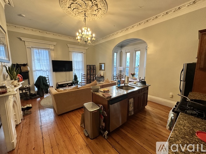 A large, empty living room with wood floors and a chandelier.