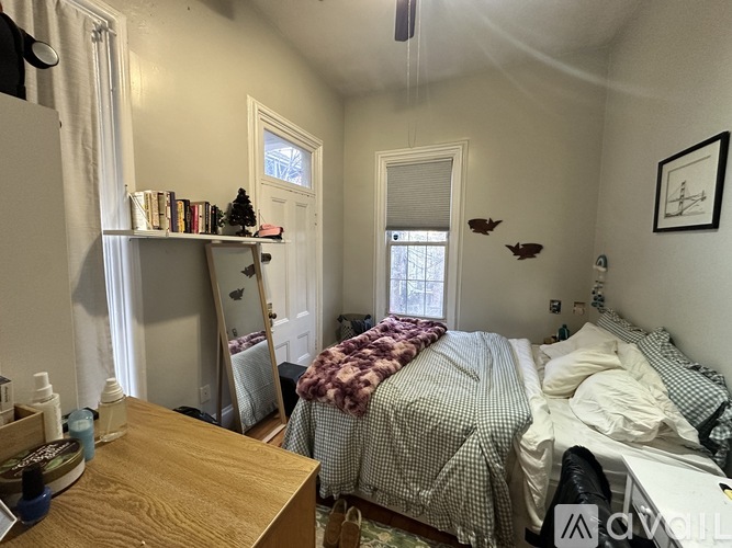 A bedroom with two beds, one with a red and white blanket, and a wooden desk with a mirror and a bottle on it.