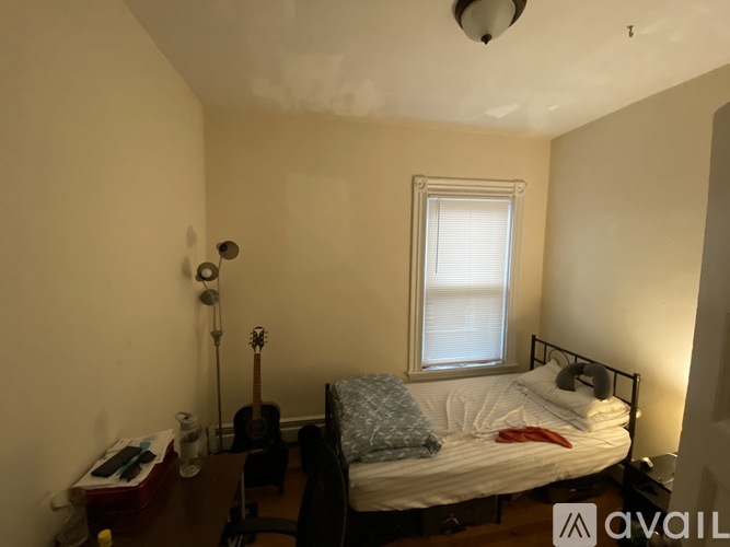 A bedroom with a bed, a guitar, a window, and a desk.