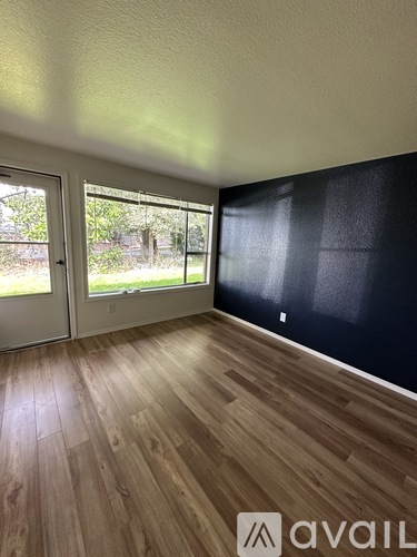 A room with wooden flooring and a large window with blinds.