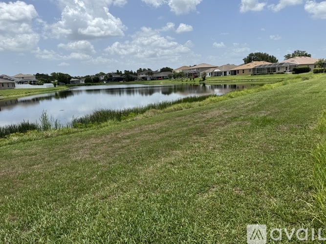 A grassy field with a lake and houses in the background.
