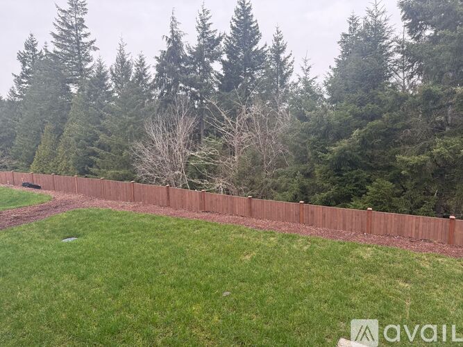 A grassy area with a fence and trees in the background.