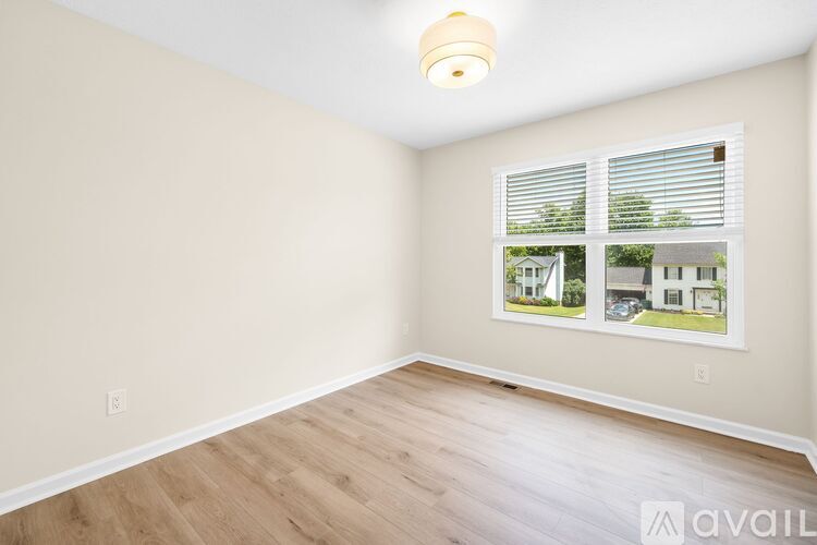 A room with a window showing a view of a house and trees.
